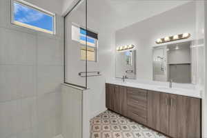 Full bath featuring tile patterned floors, tiled shower, double vanity, and a sink