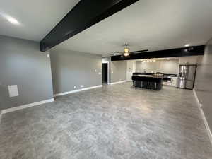 Unfurnished living room featuring a sink, beam ceiling, baseboards, and a ceiling fan