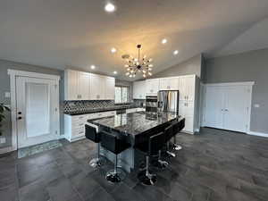 Kitchen featuring a kitchen bar, tasteful backsplash, vaulted ceiling, stainless steel appliances, and white cabinets