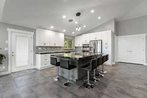 Kitchen with white cabinetry, a breakfast bar, backsplash, a kitchen island, and appliances with stainless steel finishes