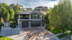 View of front facade featuring stone siding, a balcony, an attached garage, a storage unit, and driveway