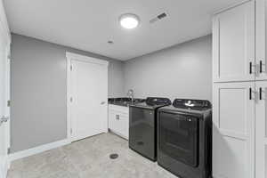 Laundry room featuring visible vents, baseboards, a sink, washer and dryer, and cabinet space