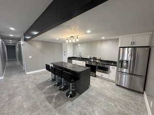 Kitchen with baseboards, white cabinetry, a kitchen island, appliances with stainless steel finishes, and a sink