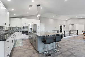 Kitchen with a kitchen bar, dark stone counters, a sink, stainless steel fridge with ice dispenser, and a center island
