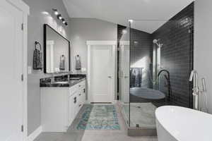 Bathroom featuring vanity, vaulted ceiling, baseboards, a soaking tub, and a stall shower