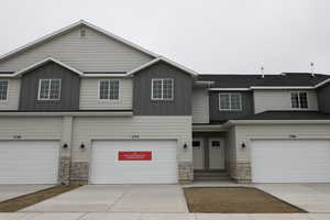 Townhome / multi-family property with stone siding, an attached garage, board and batten siding, and concrete driveway