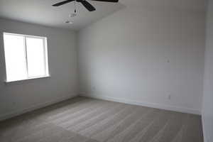 Carpeted empty room featuring visible vents, baseboards, lofted ceiling, and ceiling fan