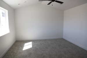 Carpeted spare room featuring a ceiling fan, baseboards, and vaulted ceiling