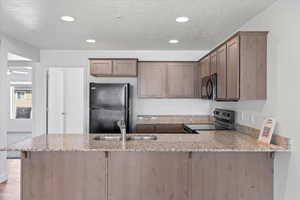 Kitchen with a sink, a peninsula, recessed lighting, black appliances, and light stone countertops