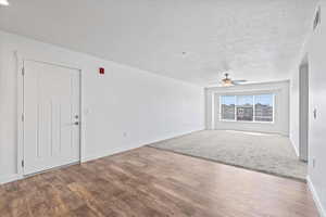 Living room with ceiling fan, a textured ceiling, wood finished floors,