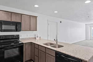 Kitchen featuring light stone countertops, a peninsula, a textured ceiling, black appliances, and a sink