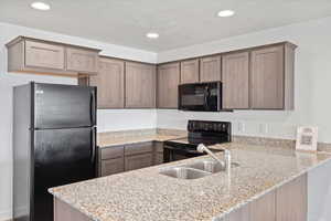 Kitchen featuring light stone countertops, a peninsula, black appliances, recessed lighting, and a sink