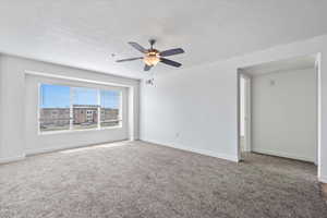 Carpeted spare room featuring a textured ceiling, ceiling fan