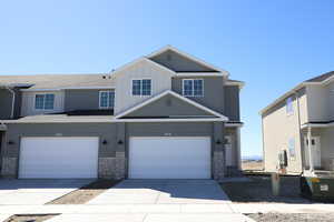View of front of house with stone siding, board and batten siding, concrete driveway, and central AC