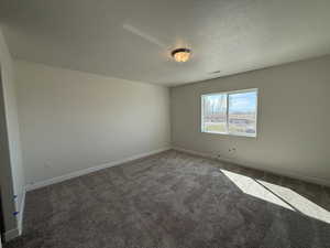Carpeted spare room with baseboards, a textured ceiling, and visible vents
