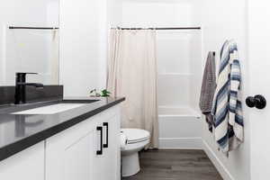 Bathroom featuring shower / bath combo with shower curtain, wood finished floors, toilet, and vanity