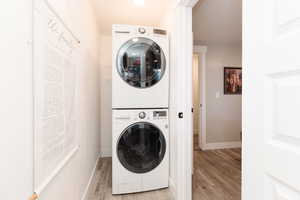 Clothes washing area featuring stacked washer / dryer, light wood finished floors, baseboards, and laundry area