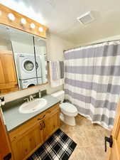 Bathroom with a textured ceiling, a shower with curtain, vanity, stacked washing machine and dryer, and light tile patterned floors