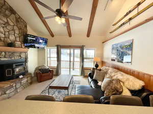 Living area featuring a wood stove, light colored carpet, beamed ceiling, ceiling fan, and high vaulted ceiling
