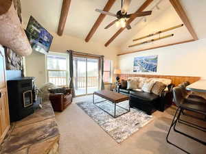 Living area with a wood stove, beam ceiling, high vaulted ceiling, carpet, and ceiling fan