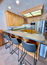 Kitchen with a kitchen bar, a textured ceiling, light countertops, a peninsula, and recessed lighting