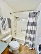 Full bath featuring washer / clothes dryer, vanity, light tile patterned floors, shower / tub combo, and a textured ceiling