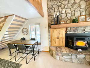 Dining room featuring a wood stove, stairway, baseboard heating, and light colored carpet
