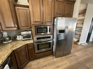 Kitchen with stainless steel appliances, light stone countertops, light wood-style floors, and baseboards