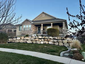 View of front of property featuring a front lawn, stucco siding, covered porch, and stone siding