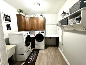 Laundry area featuring cabinet space, light wood-style flooring, washing machine and dryer, and a textured ceiling