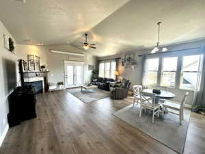 Dining space featuring a glass covered fireplace, ceiling fan with notable chandelier, vaulted ceiling, and wood finished floors