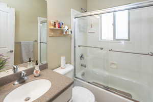 Bathroom with bath / shower combo with glass door, toilet, and vanity