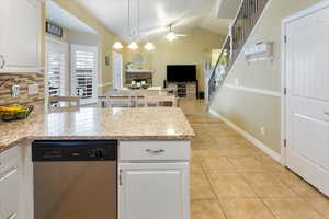 Kitchen with light tile patterned floors, ceiling fan, dishwasher, white cabinets, and a fireplace