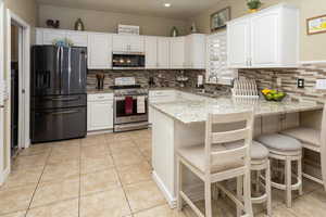 Kitchen with a sink, appliances with stainless steel finishes, a peninsula, light tile patterned floors, and white cabinets
