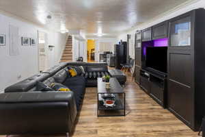 Living room featuring light wood finished floors, crown molding, stairway, and a textured ceiling