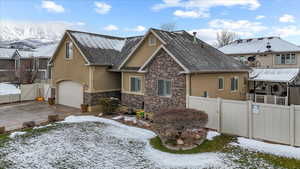 View of front of house with stucco siding, fence, stone siding, a gate, and a garage