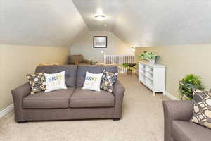 Carpeted loft featuring baseboards, lofted ceiling, and a textured ceiling