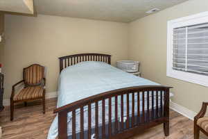 Bedroom featuring visible vents, a textured ceiling, baseboards, and wood finished floors