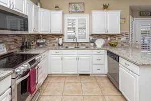 Kitchen with stainless steel appliances, backsplash, a sink, light tile patterned flooring, and a peninsula
