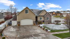 View of front of house with concrete driveway, stucco siding, fence, stone siding, and a gate
