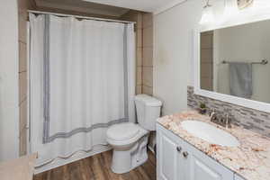 Full bath with a shower with shower curtain, toilet, vanity, backsplash, and wood finished floors