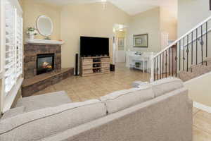 Tiled living room with stairs, a fireplace, high vaulted ceiling, and baseboards