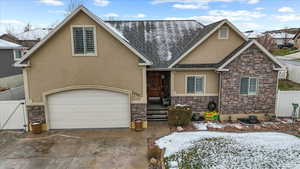 View of front facade with concrete driveway, stucco siding, roof with shingles, fence, and stone siding