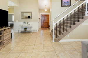 Tiled entryway with a wainscoted wall, visible vents, a towering ceiling, and stairway