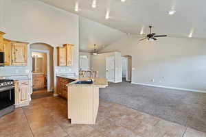 Kitchen with arched walkways, appliances with stainless steel finishes, ceiling fan, and light carpet
