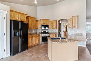 Kitchen with arched walkways, a sink, appliances with stainless steel finishes, a towering ceiling, and light stone counters
