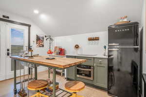 Kitchen featuring lofted ceiling, oven, butcher block countertops, freestanding refrigerator, and green cabinetry