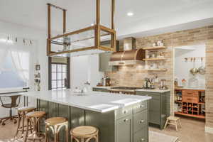 Kitchen with stainless steel gas stovetop, a kitchen island, green cabinetry, wall chimney range hood, and backsplash
