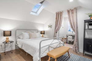 Bedroom with baseboards, vaulted ceiling with skylight, and wood finished floors