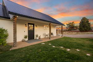 Rear view of property with stucco siding, fence, metal roof, a patio, and a yard